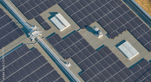 Aerial view of photovoltaic panels covering a commercial building rooftop, illustrating large-scale renewable energy generation in Livron-sur-Drome, Auvergne-Rhone-Alpes, France.