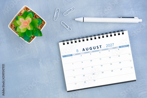 August 2027 desk calendar for 2026 and plant pot with pen on blue cement, Flat lay.