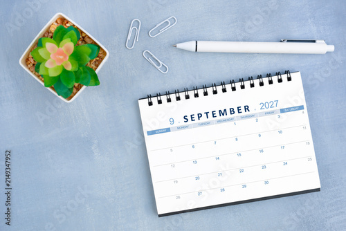 September 2027 desk calendar for 2026 and plant pot with pen on blue cement, Flat lay.