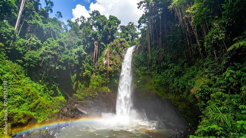 Tropical waterfall in rainforest with bright rainbow.