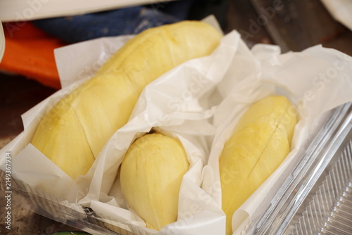 Foto Peeled Monthong durian flesh is wrapped in white paper to absorb moisture and prevent it from sticking together before being arranged in clear plastic container, ready to eat