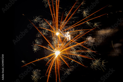 Golden fireworks display with radial orange rays and starbursts in the night sky.