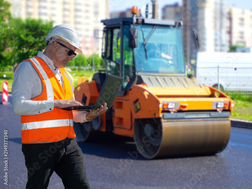 Canvastavla Road construction engineer inspecting asphalt paving beside road roller compacto