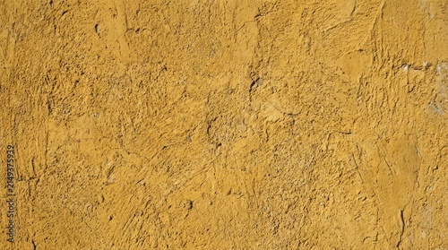 A close-up shot of a textured, ochre-colored wall. The wall surface exhibits a rough, uneven texture with visible cracks and variations in color.