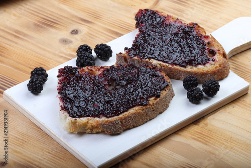 Two slices of rustic bread with thick blackberry jam and fresh berries on a white wooden board