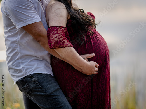 Expectant couple embracing and gently holding a pregnant belly during an outdoor maternity portrait session.