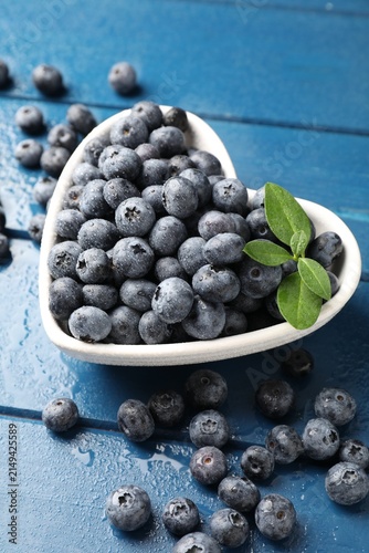 Obraz na plátně Fresh ripe blueberries with green leaves in heart shaped bowl on blue wooden tab