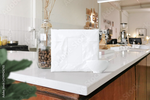 Blank white coffee pouch packaging mockup displayed on a modern kitchen counter with a softly blurred interior, ideal for coffee branding and product presentation.
