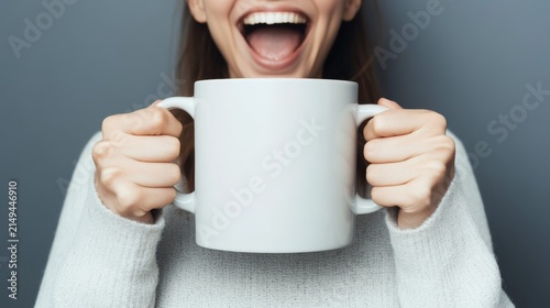 An excited woman holds a large coffee mug in her hands, with a wide smile and open mouth, showing her joy