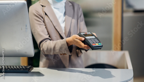 Fotografie Female receptionist employee holding card reader machine on hand at checkout counter