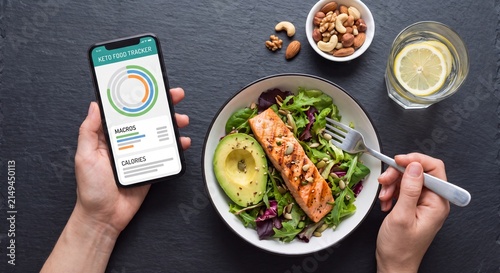 Keto diet and healthy lifestyle concept featuring a person holding a smartphone to track macros next to a grilled salmon salad meal