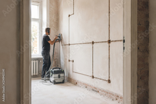 Trabajo de renovación en una habitación vacía con un trabajador usando una herramienta eléctrica en la pared