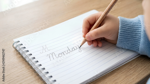 Child Writing Word Monday in Cursive on Lined Spiral Notebook Close Up Education Concept