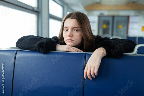 Young woman leans on a blue seat inside a commuter train