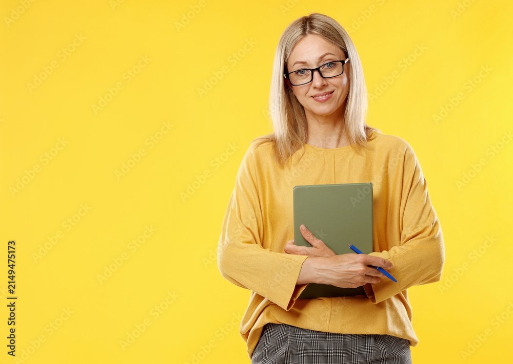 Fototapeta premium Teacher in glasses with notebook and pen on yellow background, space for text