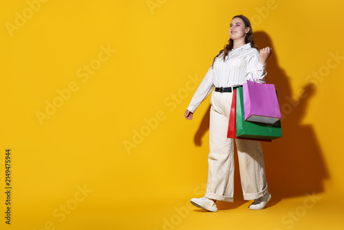 Happy overweight woman with shopping bags on yellow background, space for text