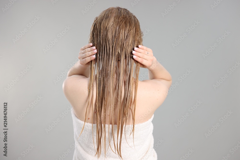 Fototapeta premium Woman applying mask onto her hair against light grey background, back view