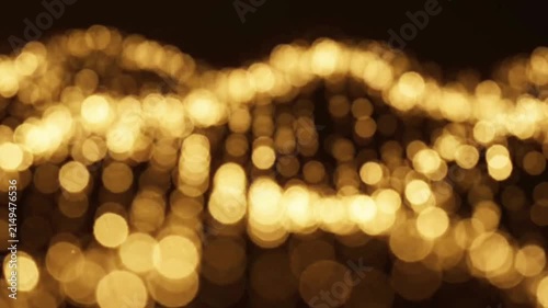 Abstract golden bokeh lights slowly wave across dark background, creating beautiful shimmering pattern, dynamic motion creates sense of wonder.