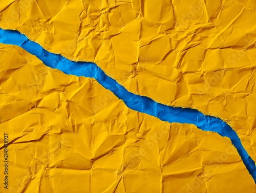 Foto Abstract background of crumpled yellow paper torn open to reveal vivid blue layer, creating strong diagonal ripped-paper texture with contrasting colors, rough edges and expressive separation concept