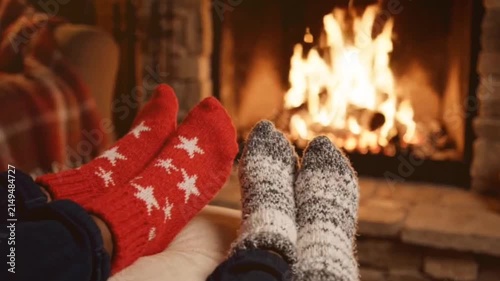 Cozy couple's feet in warm holiday socks relax by glowing fireplace on cold winter evening with soft flickering flames motion footage.
