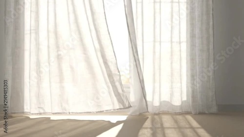 White curtains fluttering in gentle breeze against bright window in minimalist room with sunlight streaming across floor creating peaceful morning ambience.