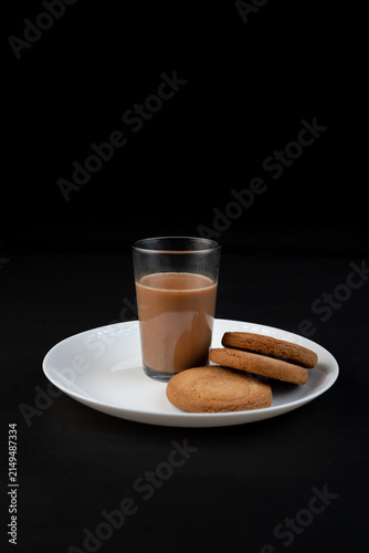 Traditional Indian tea in a clear glass and Biscuit isolated on a black background