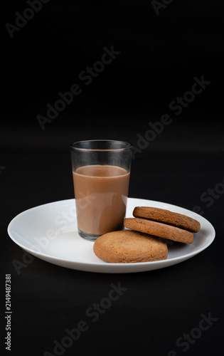 Traditional Indian tea in a clear glass and Biscuit isolated on a black background