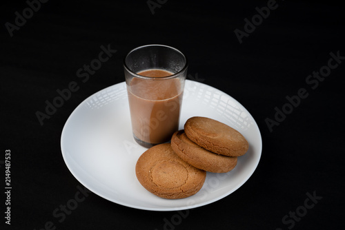 Traditional Indian tea in a clear glass and Biscuit isolated on a black background