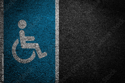 Disabled parking symbol on asphalt. Blue wheelchair sign painted on road. Accessible parking space marking outdoors. Urban street surface detail. Public accessibility infrastructure. Safety rules zone