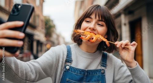 Young woman eating shrimp on a stick while taking a selfie outdoors
