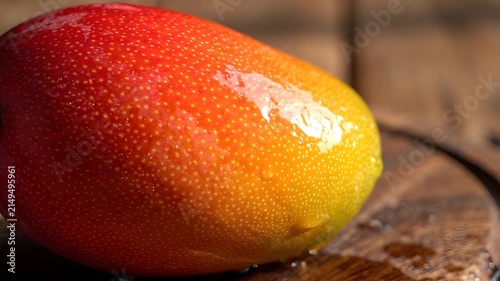Fresh ripe mango fruit with water droplets on wooden table.