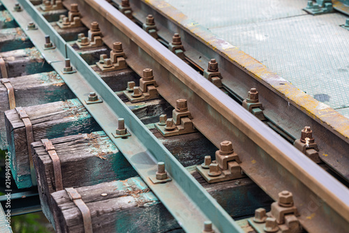 Foto Railway Tracks Close-Up With Wooden Sleepers, Bolts, Rust and Industrial Bridge