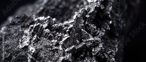 Metallic mineral specimen showing crystalline structure of raw silicon or molybdenum ore with silver shine on dark rocky background.