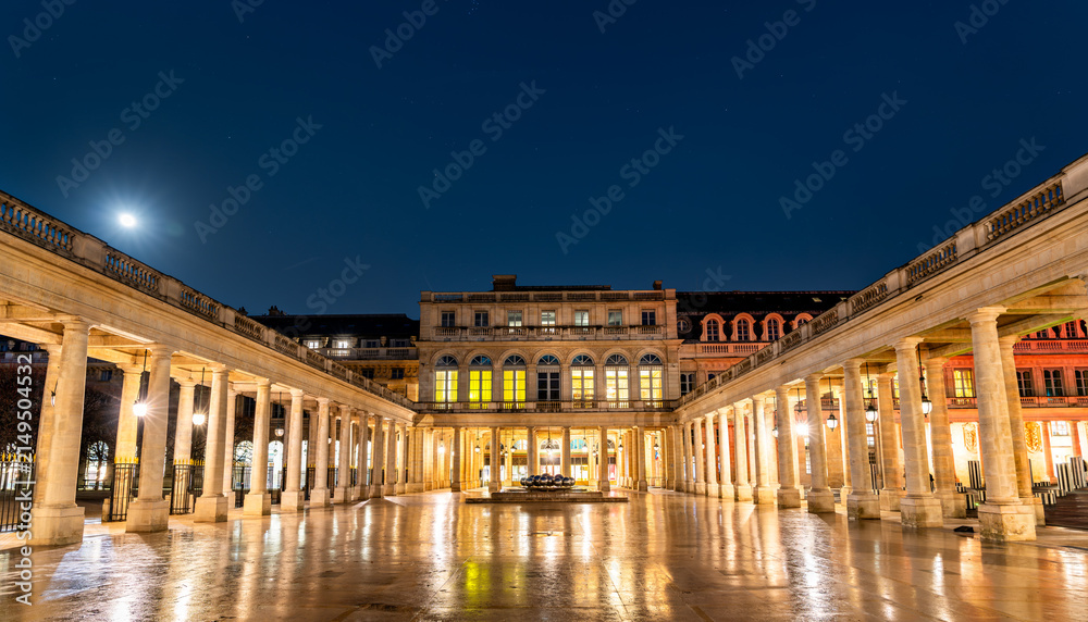Fototapeta premium Illuminated colonnades and courtyard of the historic Palais Royal at night with reflections on wet ground in Paris, France.