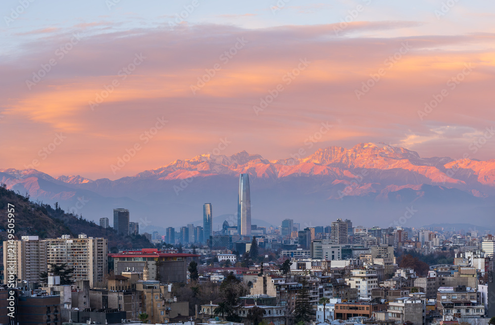 Fototapeta premium Panoramic view of Santiago de Chile city skyline at sunset with the snow capped Andes mountains under a colorful orange and pink sky
