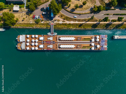 Aerial view of a river cruise ship docked at a pier on the Rhine river with white umbrellas and deck seating in Vogelgrun, Grand Est, France.