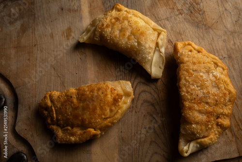 Top view close up of three freshly fried golden brown empanadas on a rustic wooden board