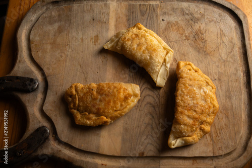 Top view of three freshly fried golden brown empanadas on a rustic wooden board