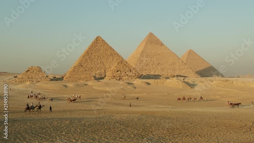 Great Pyramid of Giza with camel riding tours on sandy plateau on clear day, tourist attractions. 