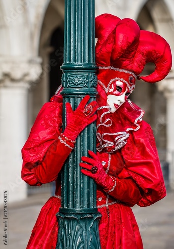 Person in red costume poses by a green lamp post in St Mark plaza during a Venice Carnival