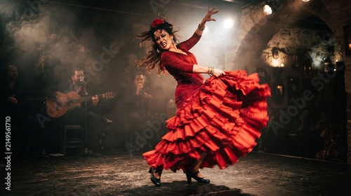 Dancer in red dress performing traditional flamenco on stage with flamenco