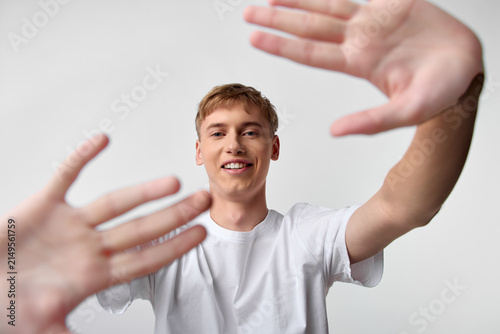 Hands reaching toward the camera with a smiling young man in a white tee creating a friendly connection, dynamic foreground gesture, conveying welcome collaboration help and active engagement in