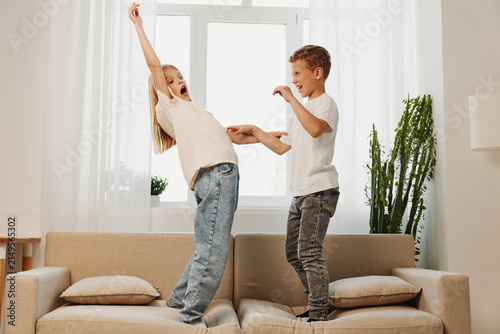 Fotografía Two happy children standing on a beige sofa in bright living room playing and laughing