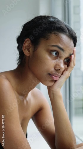 Young multiracial woman resting head on hand looking out window indoors close up shot