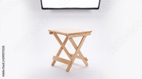 Simple Wooden Folding Stool: A compact and portable wooden stool, featuring a slatted seat and an X-frame base, stands ready for use in a clean, bright studio setting.