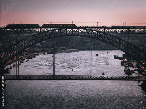 Aerial view of the iconic Luis I Bridge spanning the Douro River with a metro train crossing the upper deck and boats on the water in Porto, Porto District, Portugal.