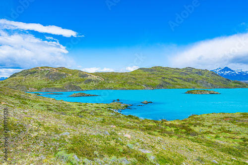Foto Brilliant azure blue waters of Lake Nordenskjöld lapping against green grassy hills beneath cloudy skies in Torres del Paine, Chile