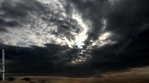 Sunset light breaks through dark storm clouds after rain creating dramatic timelapse sky scene.