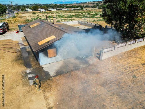 Firemen and women practicing to put out fires on an abandoned house looking at from a UAV Drone as smoke billows from the windows and roof so Fire Fighters can practice their skills