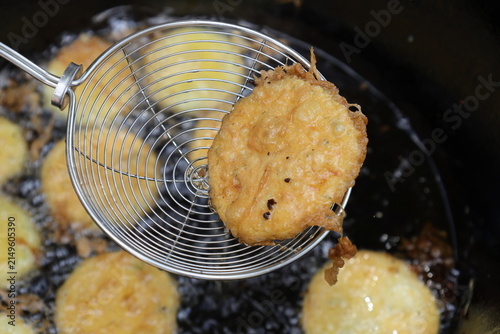 Bild auf Leinwand Crisp golden battered zucchini fritter lifted from hot oil on a wire skimmer, wi